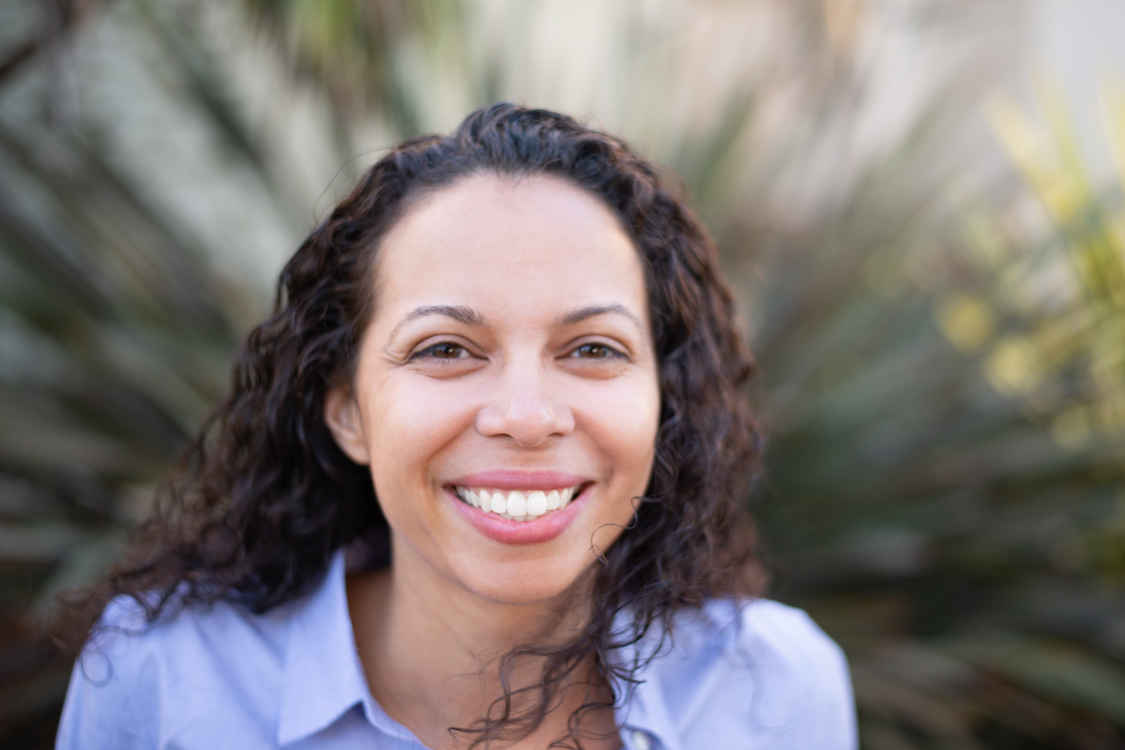 Rev. Sally Steele in a contemplative professional portrait, wearing glasses and standing outdoors with soft natural lighting
