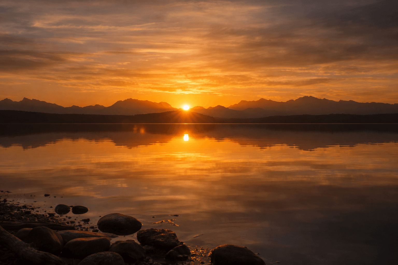 Peaceful sunrise over calm water with mountains in silhouette